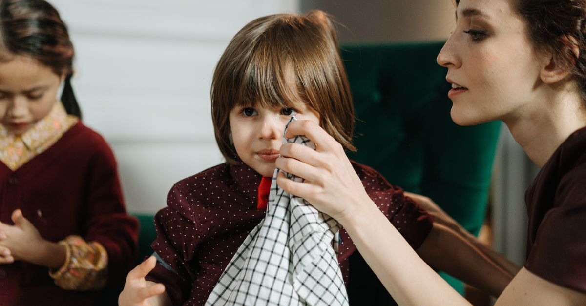 Woman assisting a child with a napkin during a meal indoors, highlighting care and family bonding.